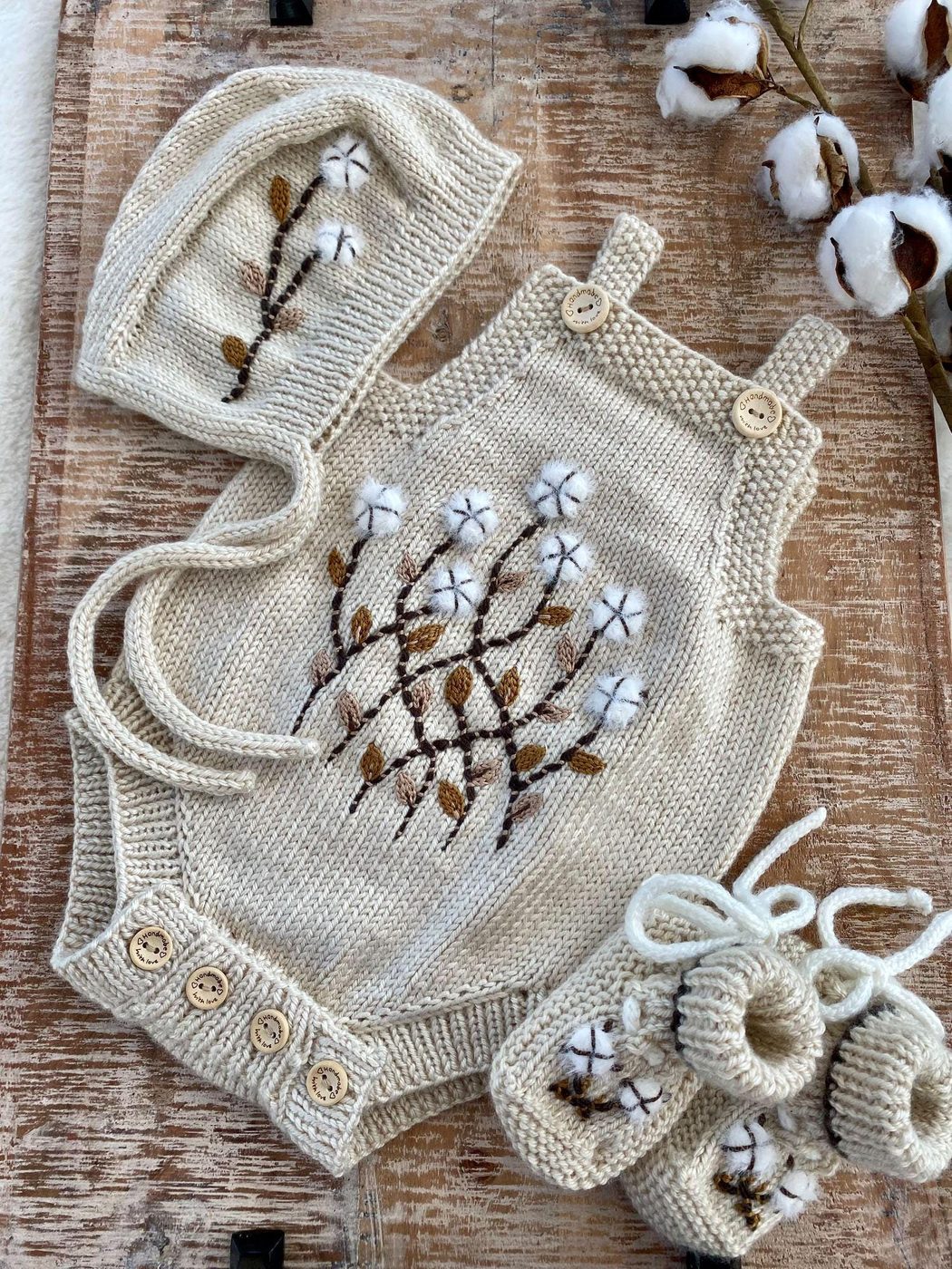 Hand-knit baby romper with matching bonnet and booties, embroidered with cotton blossoms